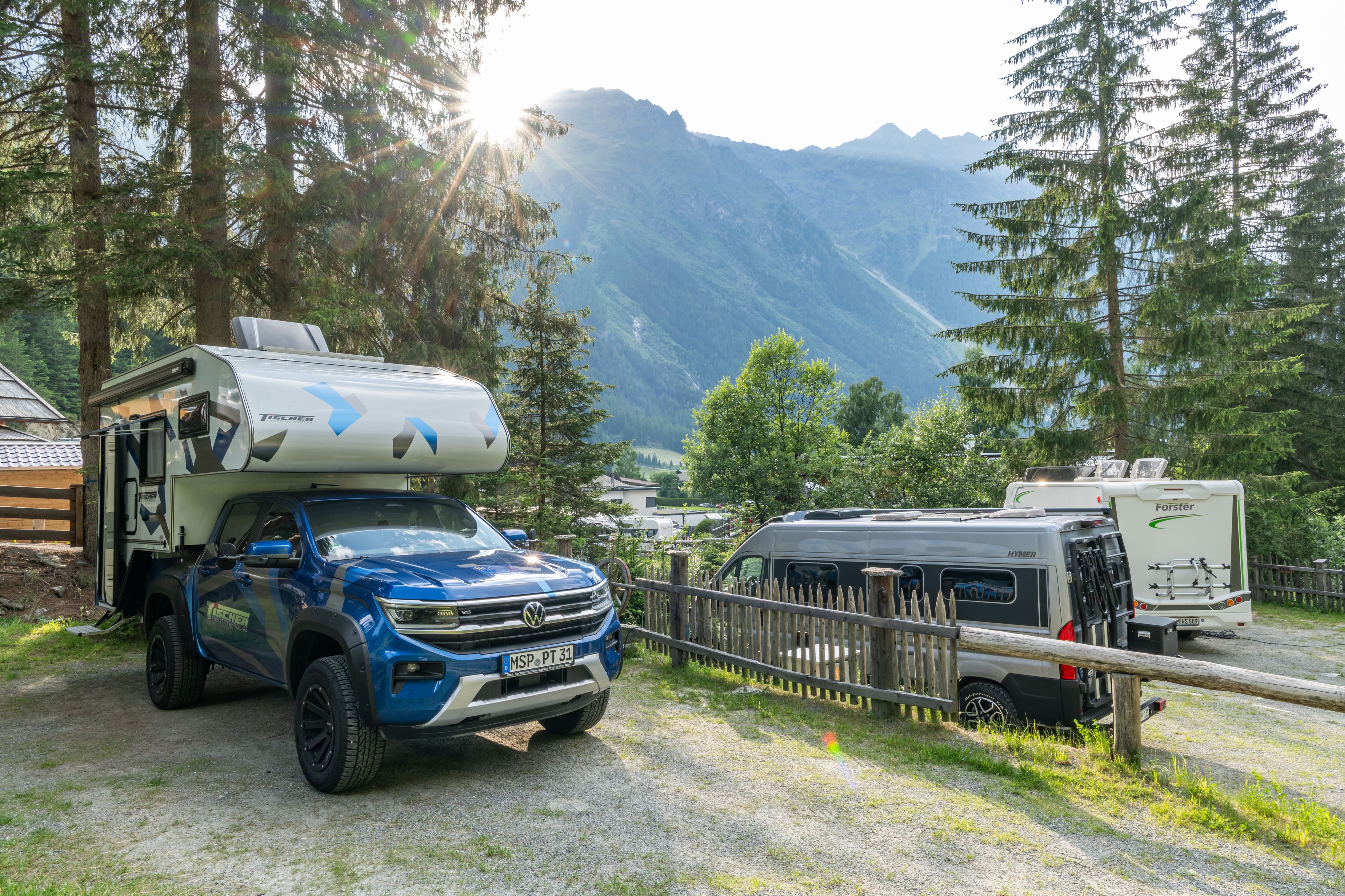 Pickup-Wohnmobil mit Absetzkabine und Campingbus auf einem Alpen-Campingplatz