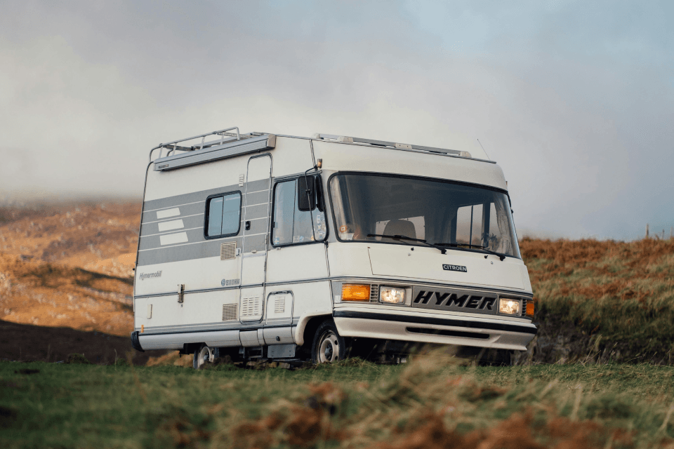 Historisches integriertes HYMER-Wohnmobil in einer grasbewachsenen Hügellandschaft.