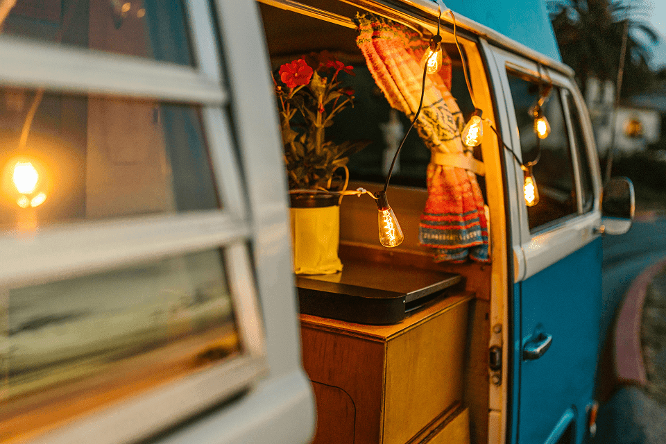 Offene Tür eines Campingbusses mit Holzinnenausbau, buntem Vorhang und warmer Lichterkette.