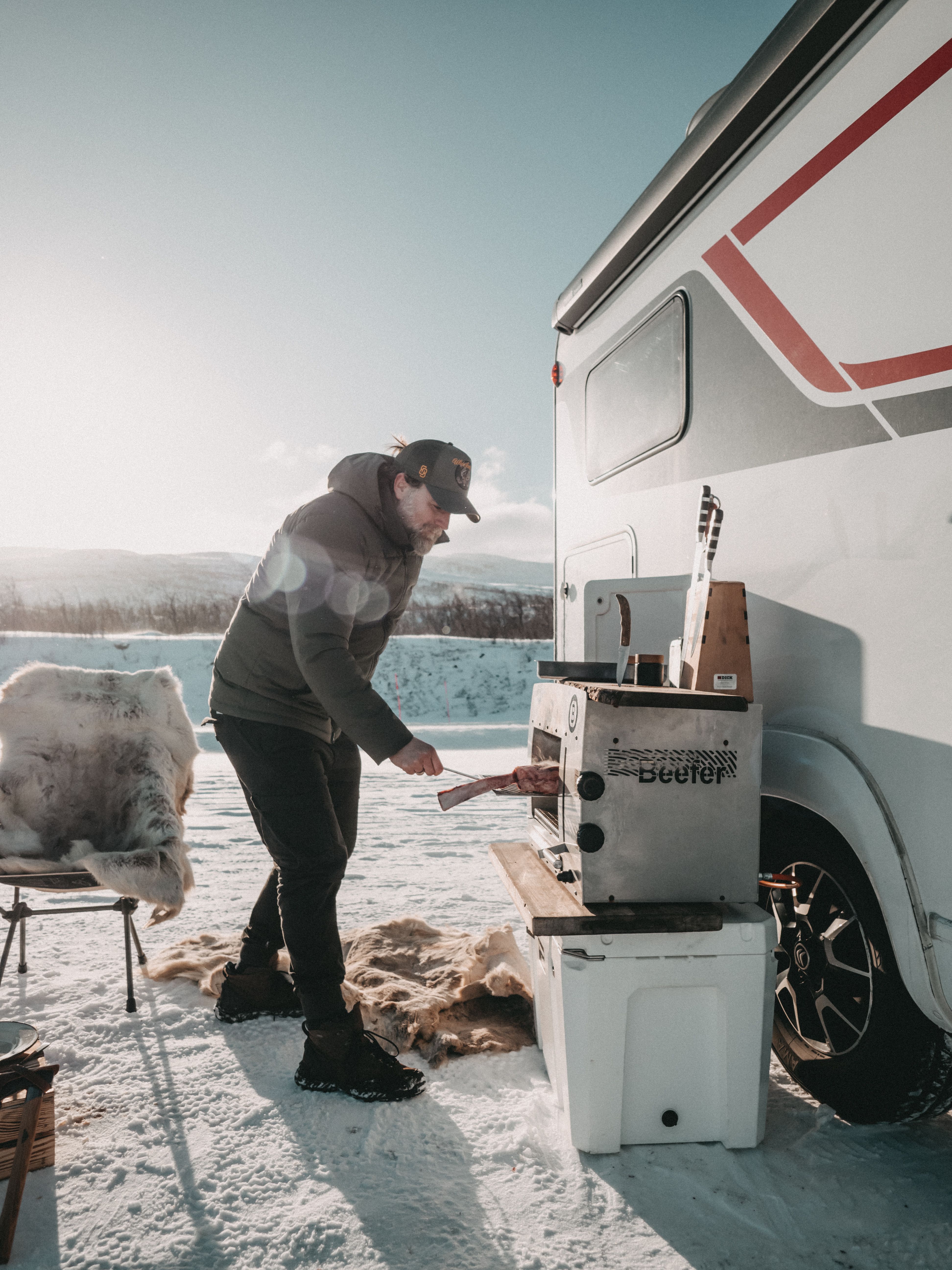 Mann grillt ein Steak an einem Beefer neben einem Wohnmobil im Schnee