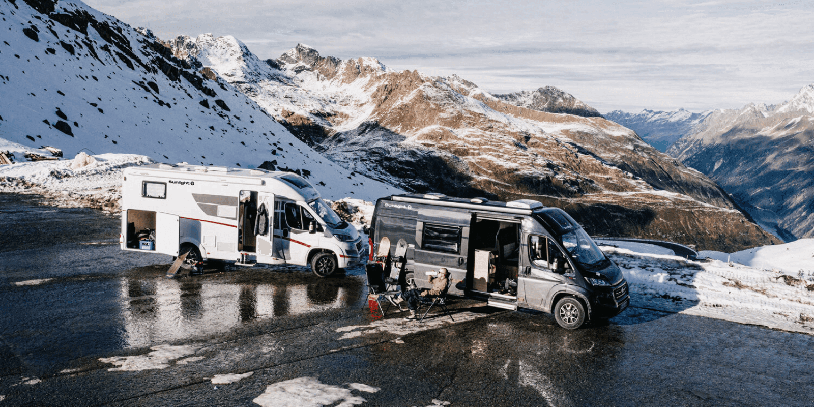 Zwei Camper stehen auf einer Straße. Davor sitzen Menschen und genießen die Sonne nach dem Wintersport.