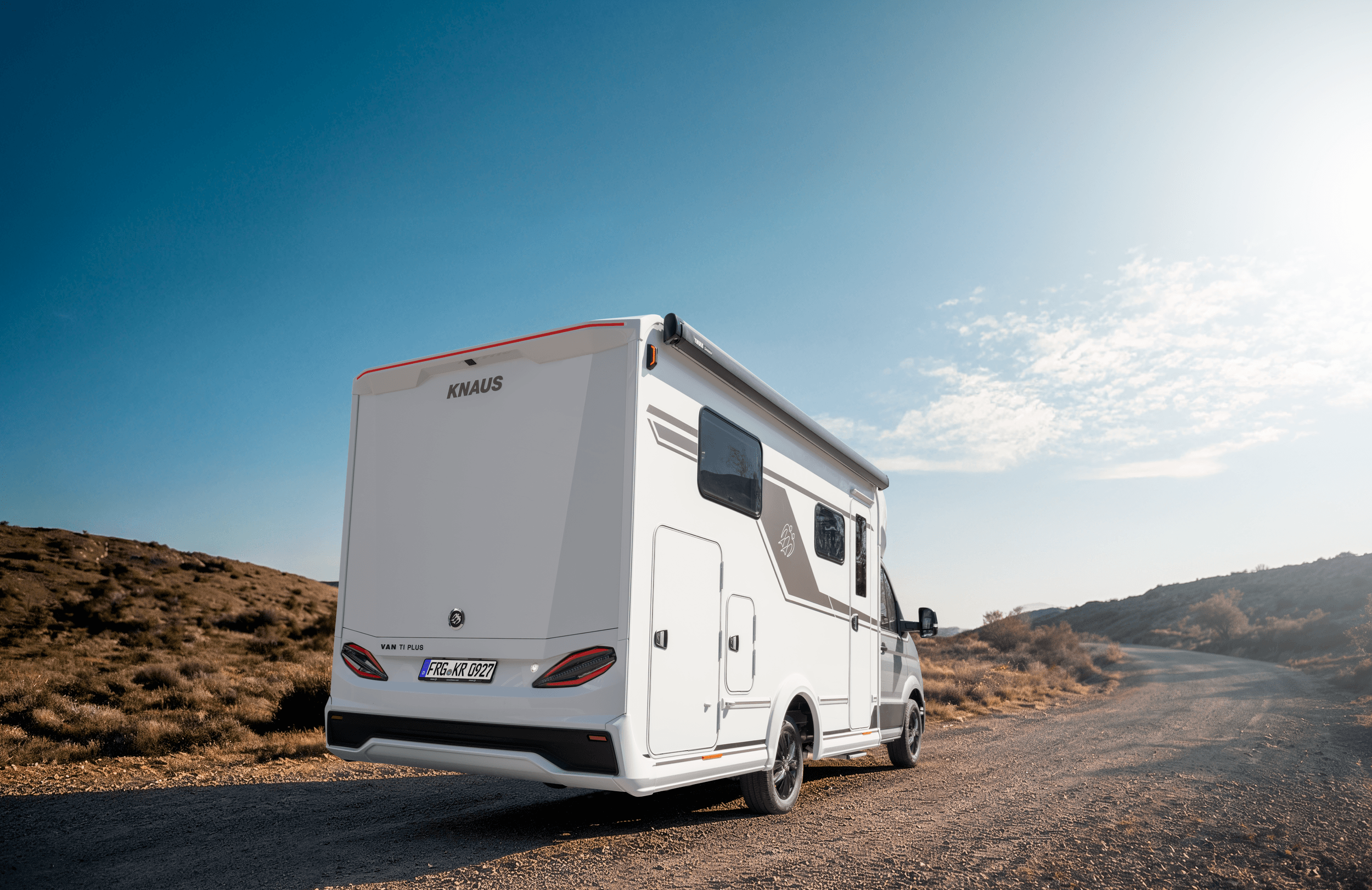 Teilintegriertes Wohnmobil Knaus Van TI Plus von schräg hinten auf einem Feldweg in weiter Hügellandschaft