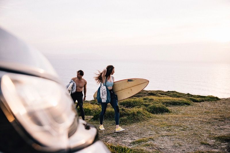 Vanlife am Meer – Paar mit Surfbrett vor dem Camper